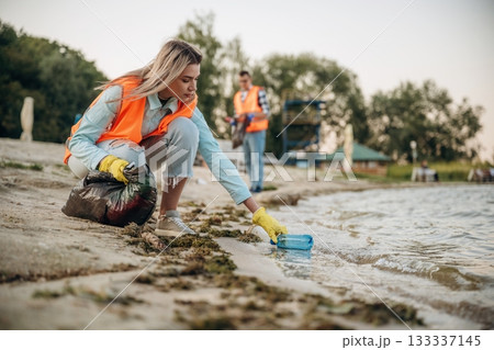 Picking bottle from the water. A volunteers collects garbage on a muddy beach 133337145