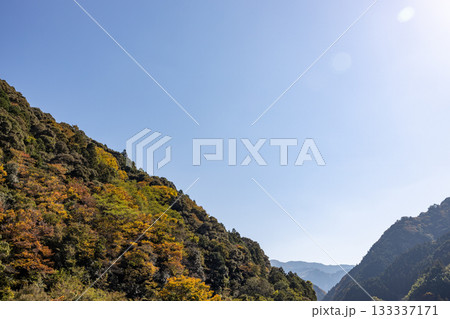秋になり少し木々が色づいてきた山と青空 133337171