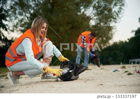 Picking up the bottle. A volunteers collects garbage on a muddy beach 133337197