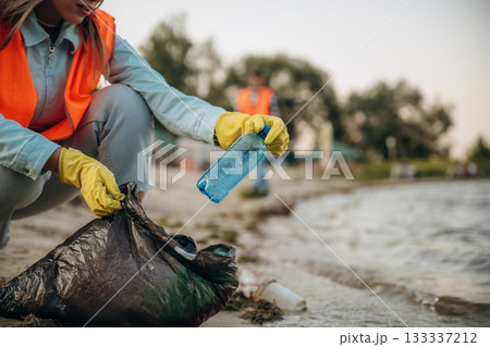 On the shore. A volunteers collects garbage on a muddy beach On the shore. A volunteers collects garbage on a muddy beach 133337212