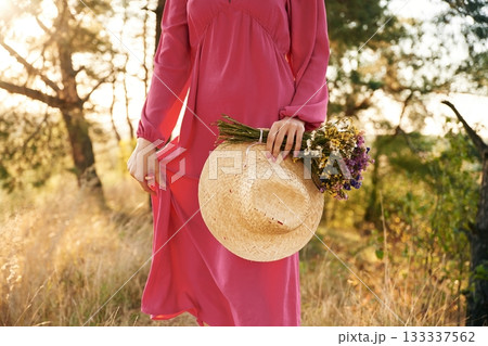 Straw hat in hand. Woman is outdoors in nature with bouquet of flowers Straw hat in hand. Woman is outdoors in nature with bouquet of flowers 133337562