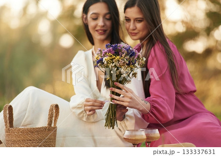 With bouquet of flowers. Lesbian couple is together on the picnic in nature 133337631