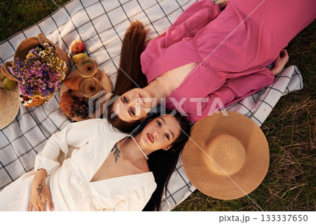Top view, lying down. Lesbian couple is together on the picnic in nature Top view, lying down. Lesbian couple is together on the picnic in nature 133337650