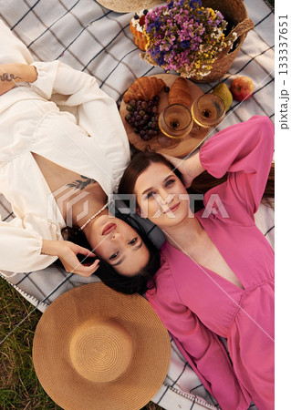 Top view, lying down. Lesbian couple is together on the picnic in nature Top view, lying down. Lesbian couple is together on the picnic in nature 133337651