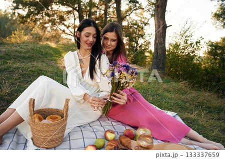 Fruits, flowers and glasses of drink. Lesbian couple is together on the picnic in nature Fruits, flowers and glasses of drink. Lesbian couple is together on the picnic in nature 133337659