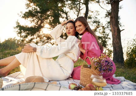 Sitting, bunch of fruits and flowers bouquet. Lesbian couple is together on the picnic in nature Sitting, bunch of fruits and flowers bouquet. Lesbian couple is together on the picnic in nature 133337685