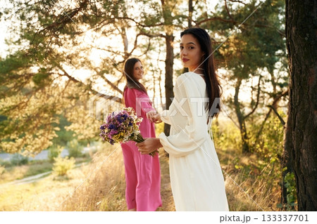 Woman is want to go, with bouquet of flowers. Lovely lesbian couple are together outdoors in nature Woman is want to go, with bouquet of flowers. Lovely lesbian couple are together outdoors in nature 133337701