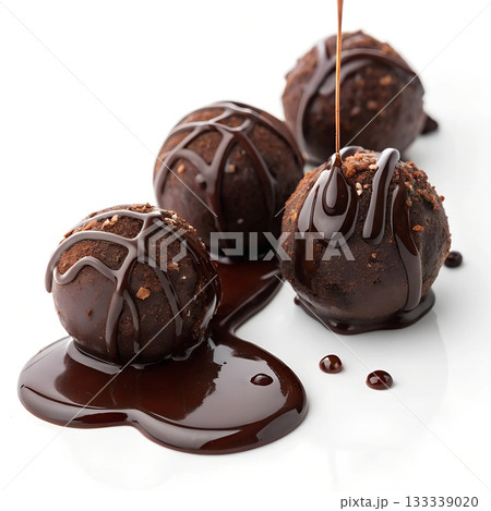 Rich dark chocolate truffles covered in chocolate drizzle and small nuts on white Rich dark chocolate truffles covered in chocolate drizzle and small nuts on white 133339020