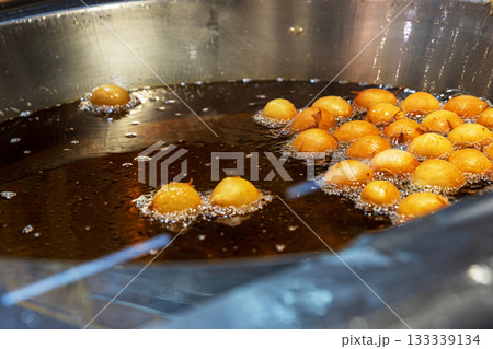 Street food vendor stirring and frying golden dough balls stirring them with metal skimmer tool, in sizzling hot oil at a winter market stall. 133339134