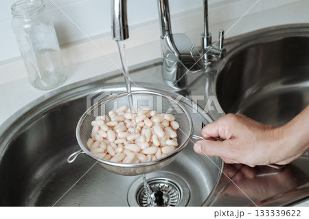man rinses cooked white beans under tap water man rinses cooked white beans under tap water 133339622