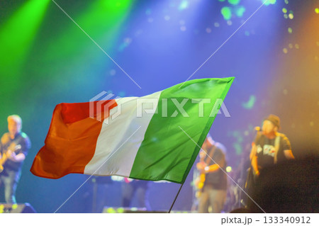 Irish tricolor flag waving at night concert during St. Patrick Day celebration, symbolizing pride and heritage. Concept of national unity, culture, festive identity 133340912