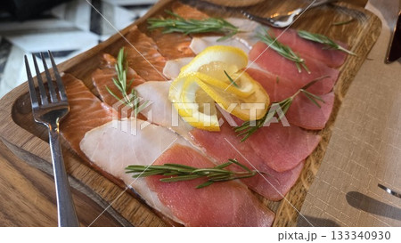 Traditional russian dish with smoked fish, lemon slices, and rosemary garnish on wooden serving board. Traditional Russian fish appetizer. Close-up 133340930