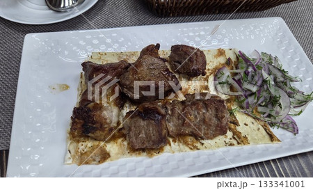 Traditional georgian cuisine dish with grilled meat and fresh herbs on a plate. Shashlik. Top view Traditional georgian cuisine dish with grilled meat and fresh herbs on a plate. Shashlik. Top view 133341001