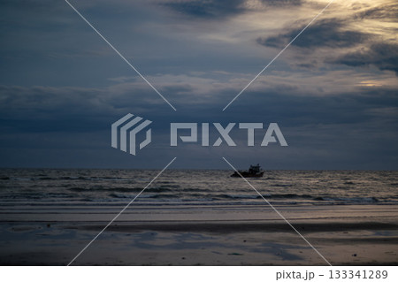 A serene and peaceful beach scene of a lone boat and gentle waves under a cloudy evening sky after a monsoon storm 133341289