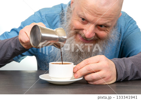 An elderly man with a long beard smiles while pouring hot coffee into a white cup 133341941