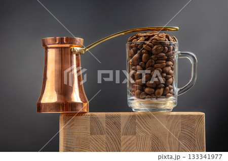 A traditional copper cezve and a glass mug filled with roasted coffee beans A traditional copper cezve and a glass mug filled with roasted coffee beans 133341977