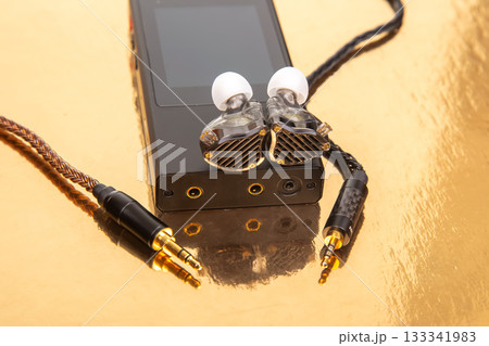 A pair of wired earbuds with a woven cable on a black music device A pair of wired earbuds with a woven cable on a black music device 133341983