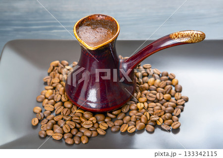 Artistic shot of a cezve with rich Turkish coffee on a gray surface, accented by roasted beans 133342115