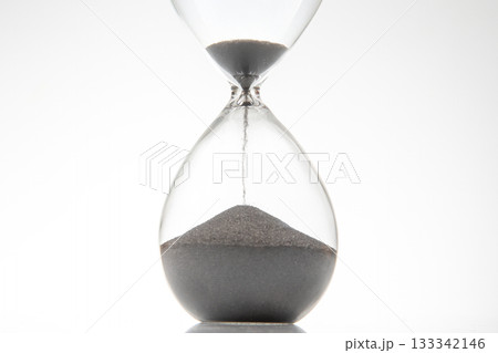 Minimalist hourglass with black sand trickling down on a white backdrop Minimalist hourglass with black sand trickling down on a white backdrop 133342146