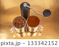 A manual coffee grinder sits between two glass mugs, one with roasted coffee beans 133342152