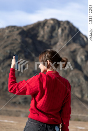 Woman in Red Sweater Capturing Scenic Mountain View with Phone Woman in Red Sweater Capturing Scenic Mountain View with Phone 133342298