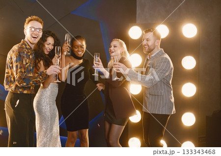 Young women with a hairstyle in an elegant outfits and man in costumes holding a ballons in shape of numbers 2022. Women standing in the decorated interior of the house during the Christmas holiday Young women with a hairstyle in an elegant outfits and man in costumes holding a ballons in shape of numbers 2022. Women standing in the decorated interior of the house during the Christmas holiday 133343468