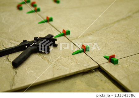 To achieve a flawless wall surface, the tiler employs a lash system, placing clips and wedges between tiles to keep them level while the adhesive cures completely. 133343596