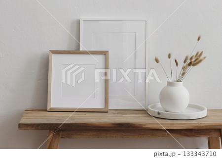 Minimalist home decor scene. Two blank picture frames. Wooden bench, table, white ceramic vase with dried lagurus flowers. Modern neutral interior mockups for artwork, prints, posters. Branding. 133343710