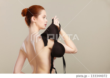 Naked woman holds black bra in hand Naked woman holds black bra in hand 133344072