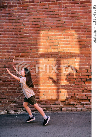Child girl running chasing shadow on brick wall 133345595