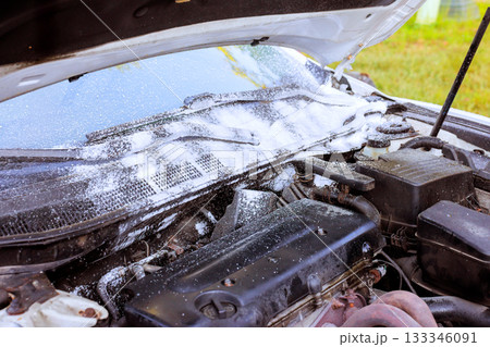 Mechanic uses foam to clean engine compartment of car under hood Mechanic uses foam to clean engine compartment of car under hood 133346091