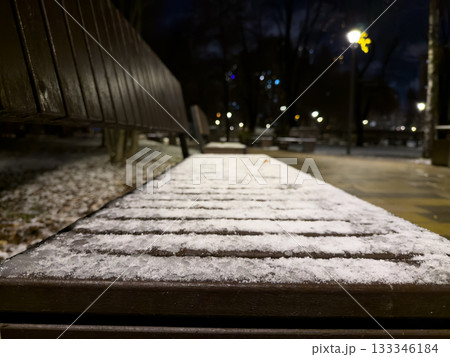 Close up photo of frozen bench in park at night. Snow completely covered the wooden bench in the city promenade. The park after the first snowfall, with frozen benches covered in snow Close up photo of frozen bench in park at night. Snow completely covered the wooden bench in the city promenade. The park after the first snowfall, with frozen benches covered in snow 133346184