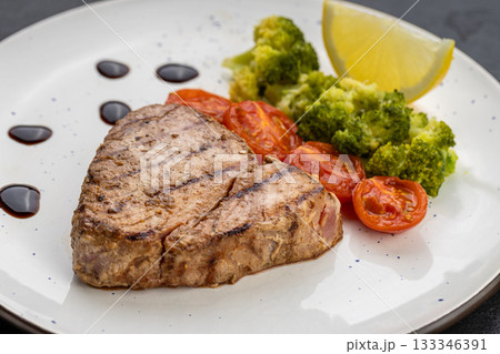 Grilled tuna steak with broccoli, cherry tomatoes and lemon on a white plate Grilled tuna steak with broccoli, cherry tomatoes and lemon on a white plate 133346391