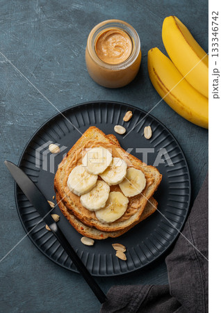 Peanut butter toast and banana on a black plate on a dark background with nuts Peanut butter toast and banana on a black plate on a dark background with nuts 133346742