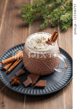 Hot chocolate and wipped cream in a cup on black plate with spices on a wooden background Hot chocolate and wipped cream in a cup on black plate with spices on a wooden background 133346757