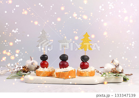 Christmas and New Year's dishes, a set of appetizers for the festive table. Canapes with soft mozzarella cheese, grapes, and olives on a marble table, Christmas Eve concept Christmas and New Year's dishes, a set of appetizers for the festive table. Canapes with soft mozzarella cheese, grapes, and olives on a marble table, Christmas Eve concept 133347139