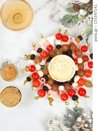 Christmas and New Year's dishes, a set of snacks and refreshing drinks for the festive table. A plate with canapes of tomatoes, mozzarella cheese, olives, black olives and grapes on a marble table Christmas and New Year's dishes, a set of snacks and refreshing drinks for the festive table. A plate with canapes of tomatoes, mozzarella cheese, olives, black olives and grapes on a marble table 133347141