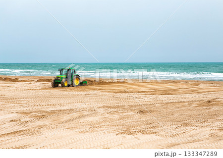 Spain, Valencia, March 29, 2024: Tractor Leveling Sand on a Beach by the Ocean on a Clear Day 133347289