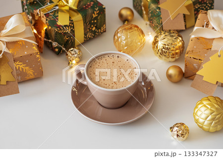 Cup of Hot Drink with Christmas Gifts and Ornaments in Cozy Holiday Setting against Christmas Tree and Lights 133347327