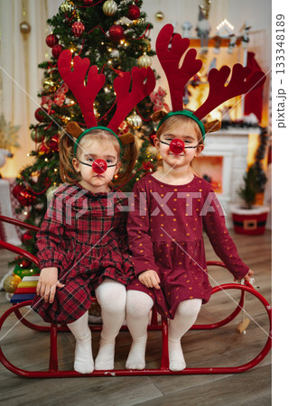 Little girls wearing reindeer costumes sitting on sled Little girls wearing reindeer costumes sitting on sled 133348189