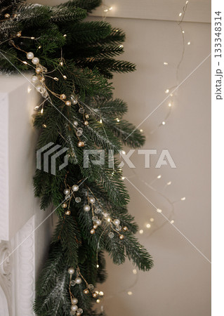Christmas garland with lights and pearls on white fireplace and beige wall Christmas garland with lights and pearls on white fireplace and beige wall 133348314