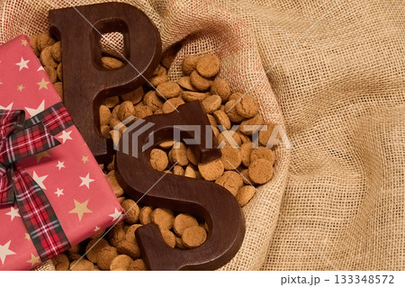 Festive Sinterklaas Treat. Chocolate letters and cookies on burlap with a wrapped gift 133348572