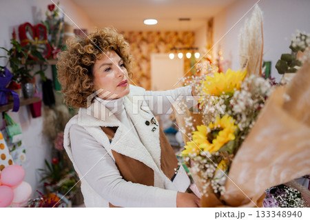 Woman arranging fresh flowers in a cozy flower shop during a bright afternoon 133348940