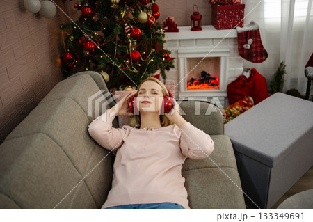 Relaxing by the holiday tree with headphones, enjoying the warmth and joy of the festive season in a cozy living room Relaxing by the holiday tree with headphones, enjoying the warmth and joy of the festive season in a cozy living room 133349691