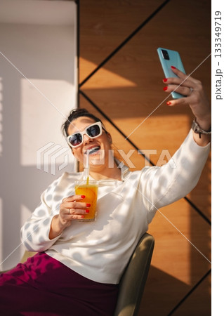 Joyful woman taking a selfie with a colorful drink in hand 133349719