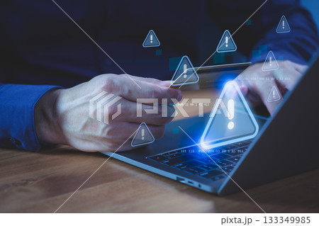 Person holding a credit card while using a laptop computer with warning symbol, representing online payment risk, online shopping, financial fraud, and identity theft during digital transactions. Person holding a credit card while using a laptop computer with warning symbol, representing online payment risk, online shopping, financial fraud, and identity theft during digital transactions. 133349985
