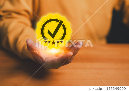 Quality assurance and customer satisfaction concept with glowing check mark badge and five star rating symbol in a person hand, representing trust, certification, service excellence and reliability. 133349990