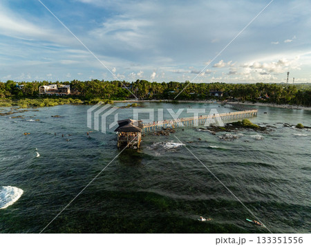 Wooden pier stretching into the ocean with surfers riding waves near the shore. Siargao, Philippines. 133351556