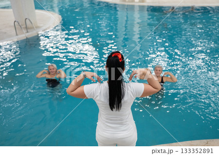 Instructor leading aquatic fitness training for group senior women in a swimming pool. Concept of health, exercise, wellness, water therapy, and active aging lifestyle Instructor leading aquatic fitness training for group senior women in a swimming pool. Concept of health, exercise, wellness, water therapy, and active aging lifestyle 133352891