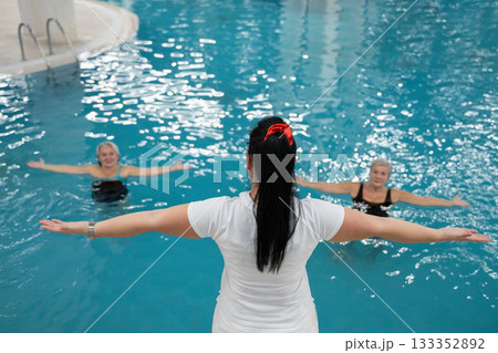 Instructor leading aquatic fitness training for group senior women in a swimming pool. Concept of health, exercise, wellness, water therapy, and active aging lifestyle 133352892
